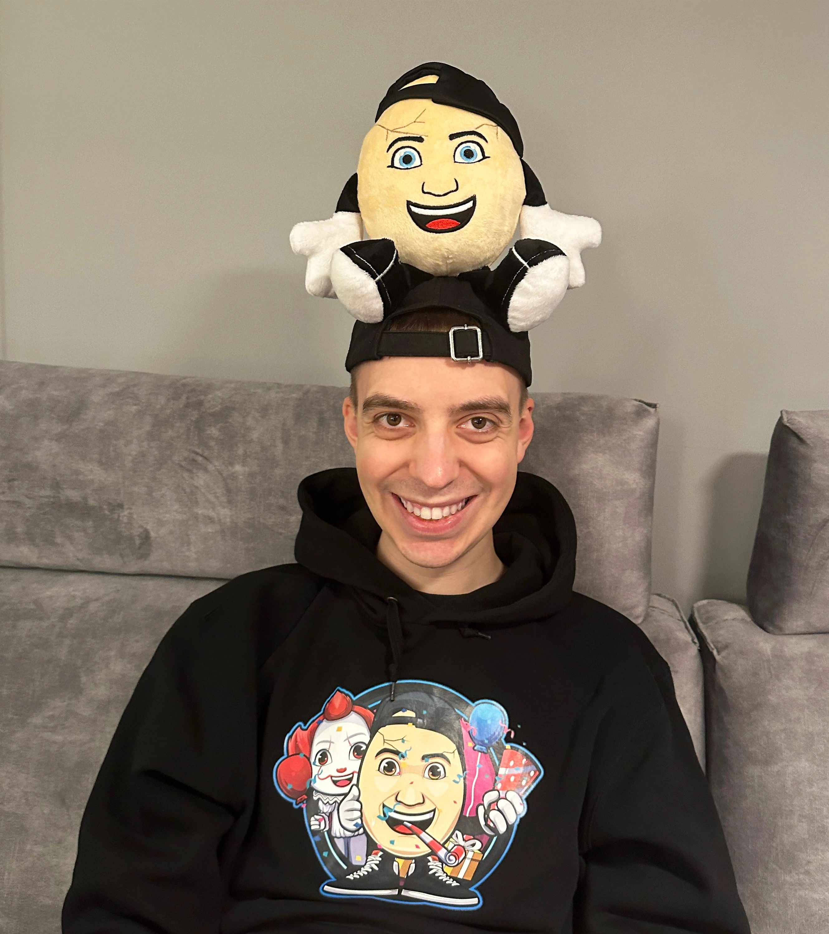 YouTuber Clashi trägt einen ClashGames-Hoodie mit buntem Print und balanciert sein eigenes Plüschtier lässig auf dem Kopf – perfekte Kombination für echte Fans.